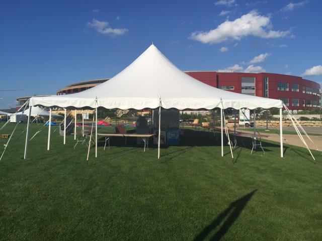 Many pole tent rentals outside on a lawn in front of a large stadium.