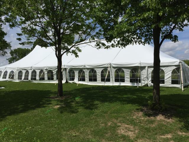 White pole tent with arch windows on a lawn with trees at an outdoor event.