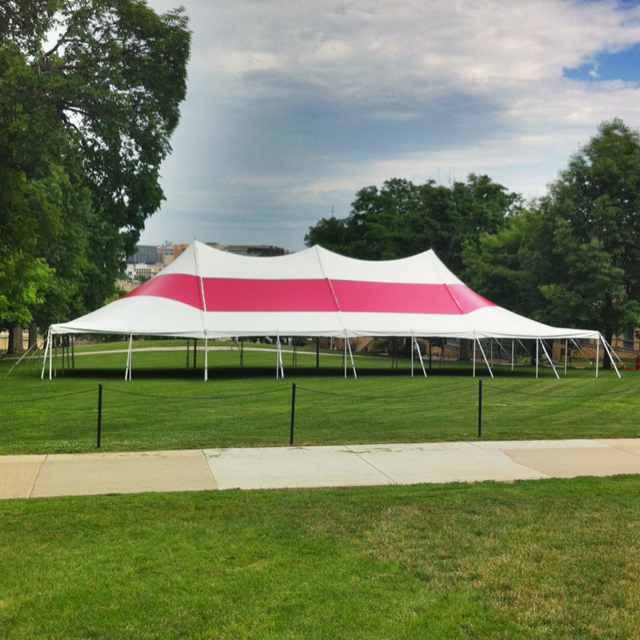 White and red pole tent in a park with a concrete walk path and a black rope chain fence.