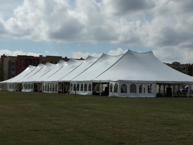 Large white pole tent with windows, set up in a field at an outdoor venue.