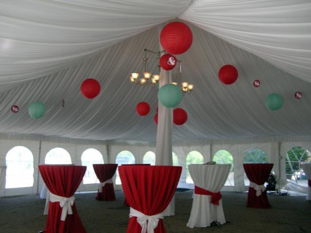 Many red and white round tables, under a white pole tent with red and turquoise paper lanterns hanging from the ceiling.