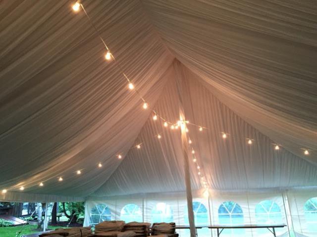 Pole tent decorated with ceiling drapes and string lights.