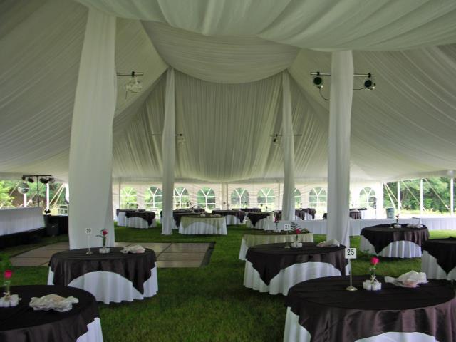 Round tables and a dance floor event rental on a lawn, under a white pole tent with ceiling drapes.