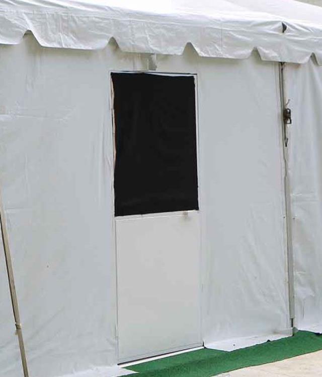 White pole tent with door, set up on turf.
