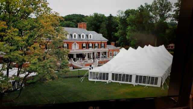 A white Pole tent set up on a lawn in front of a large brick house.