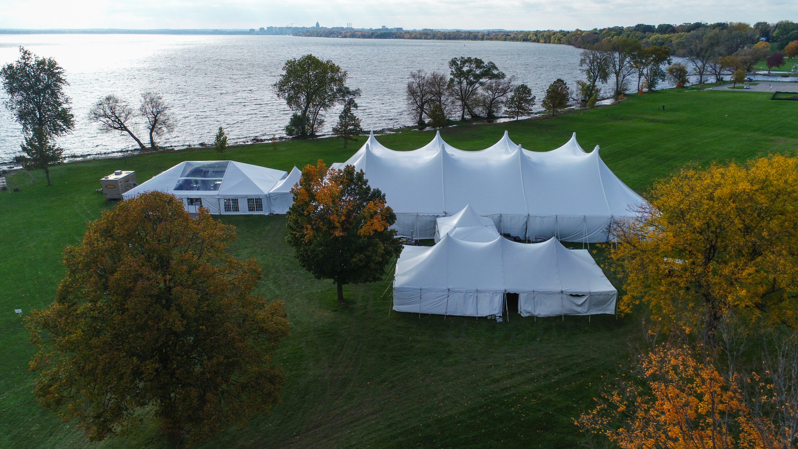 White pole tent rentals and a frame tent rental set up in a field next to a lake, for an outdoor picnic in the park event.