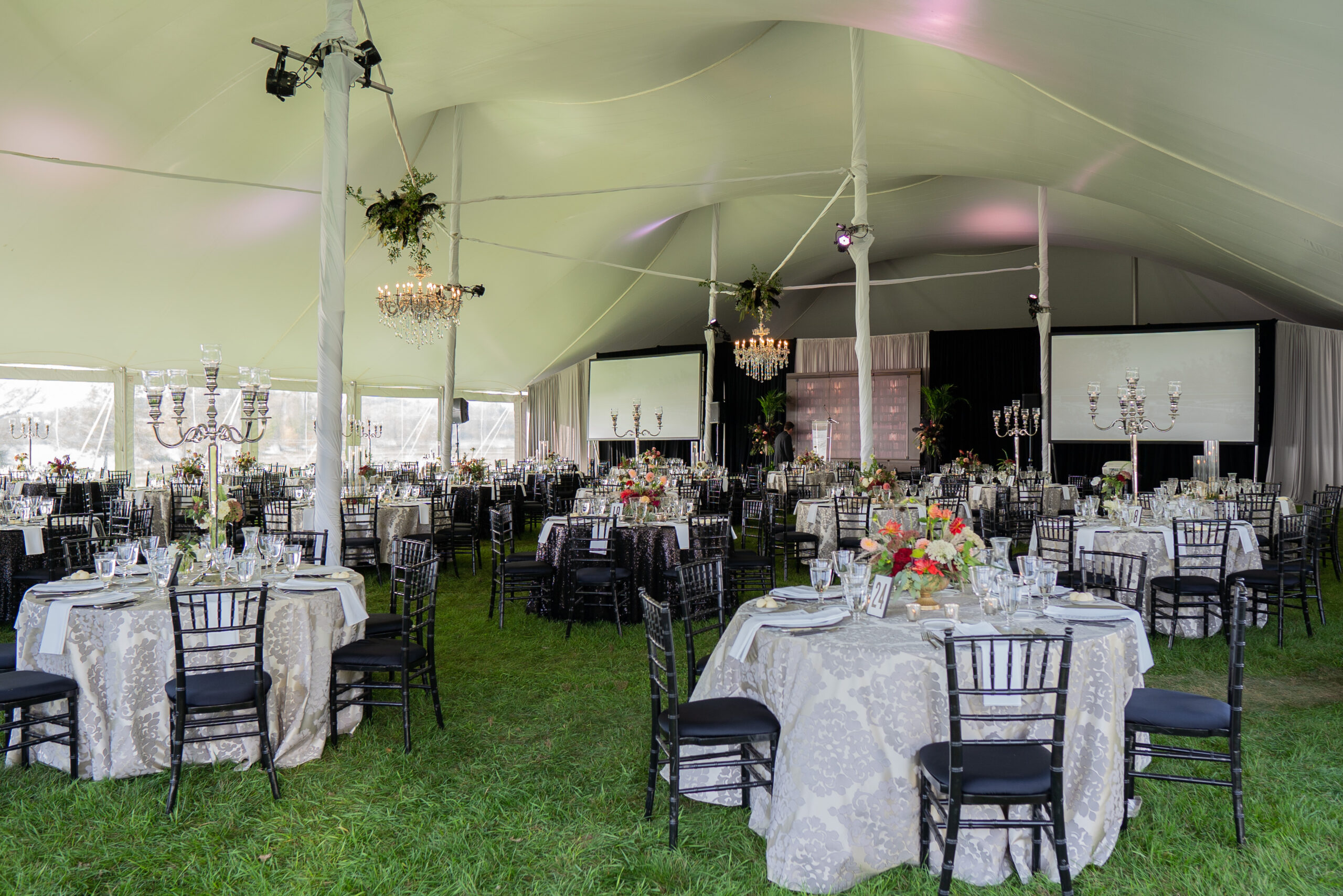 Banquet seating, a stage rental, and projector screens under a pole tent for a picnic in the park in Madison, WI.