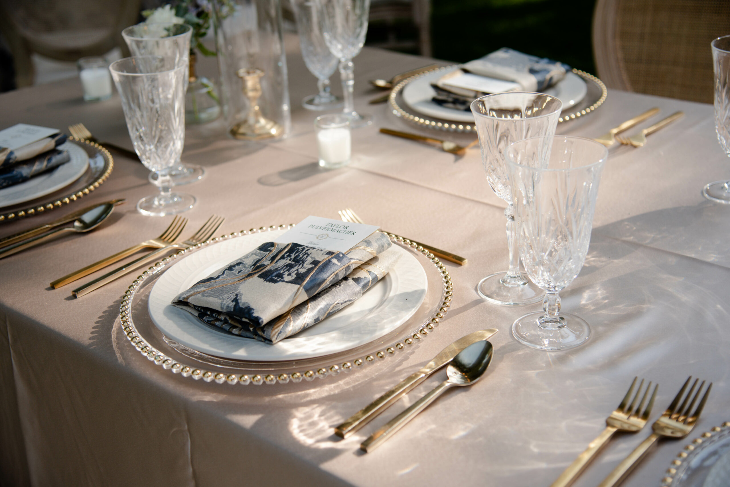Gold silverware and dinnerware rentals set at a table for a wedding dinner reception, with name tags for each guest.