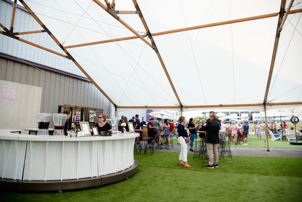 Bartenders serve event guests from a white circular bar rental at an outdoor venue. 