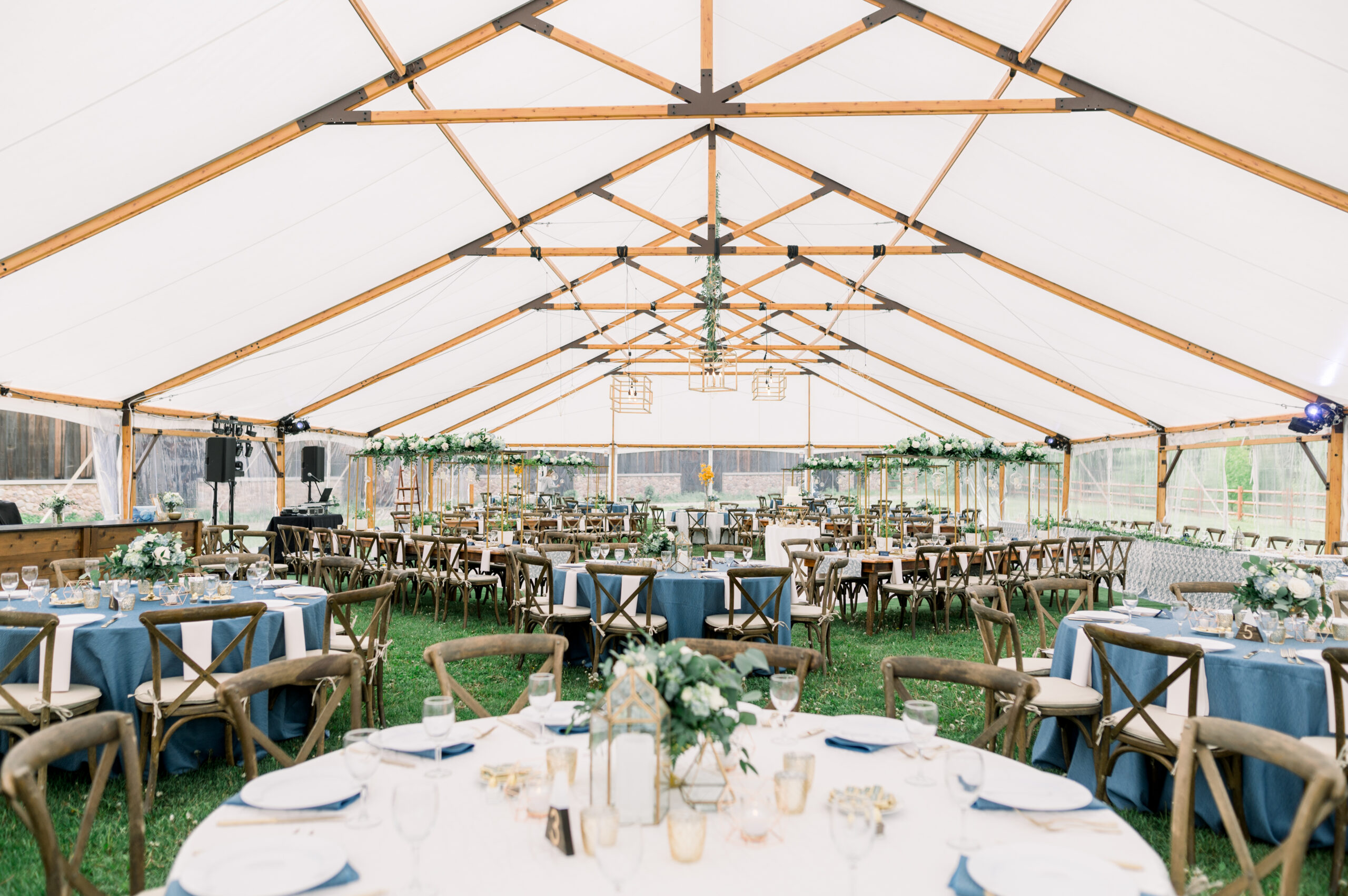 Banquet seating on a lawn for a wedding dinner reception, under a frame tent decorated with greenery.