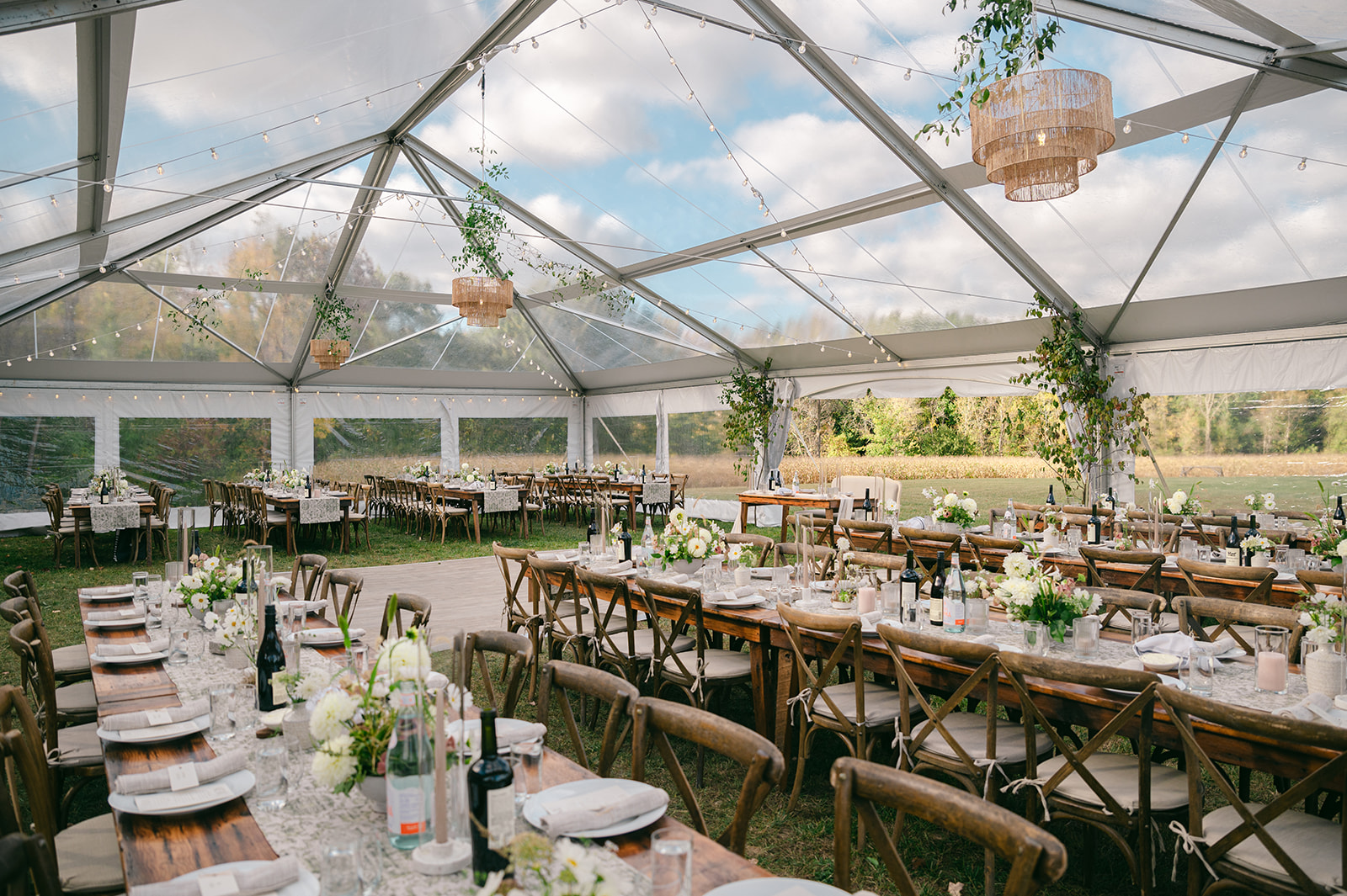 Clear frame tent set up in a field. Long tables are set for a wedding reception with a wooden dance floor in the middle.